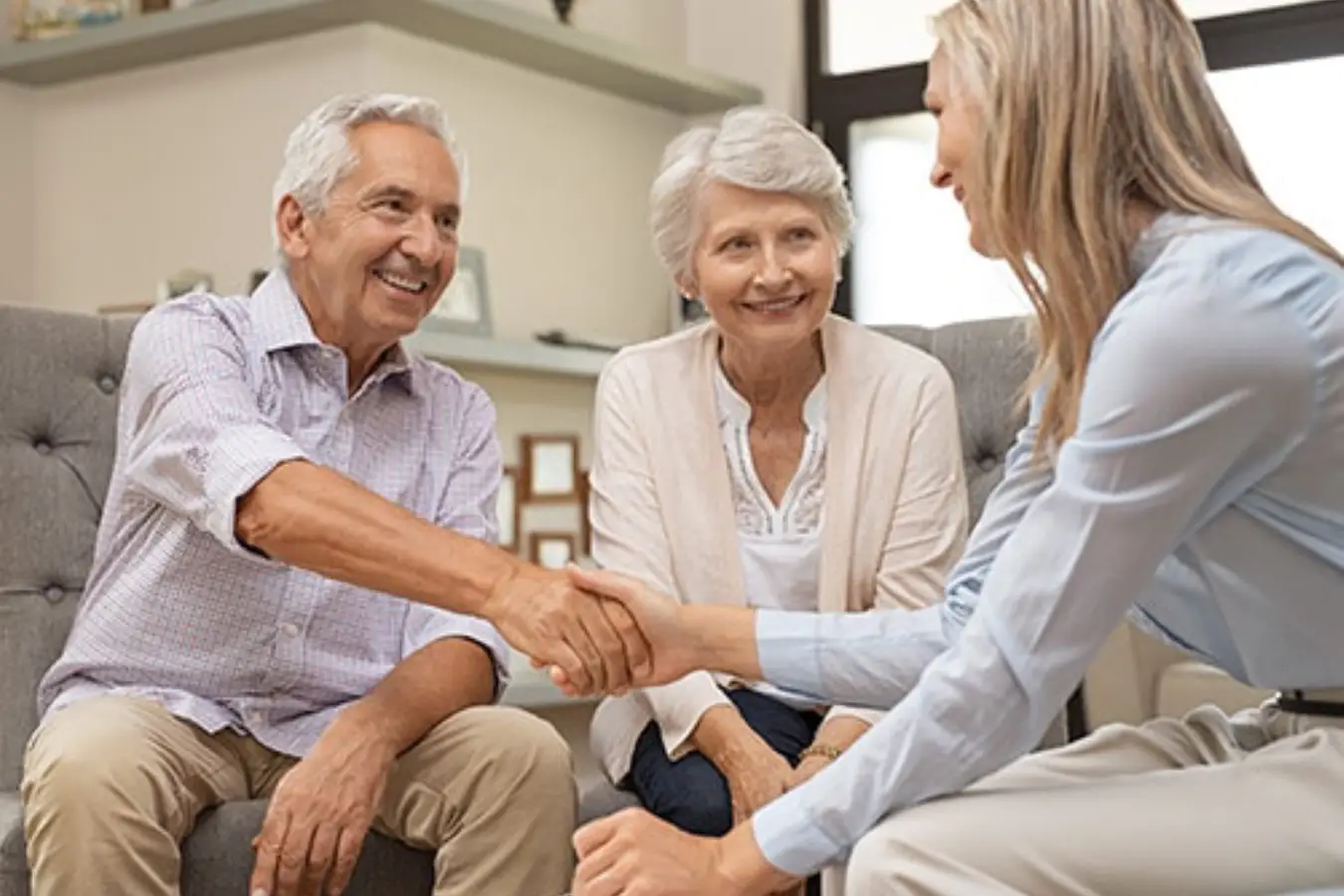 An elderly couple and a professional woman shaking hands while seated in a living room