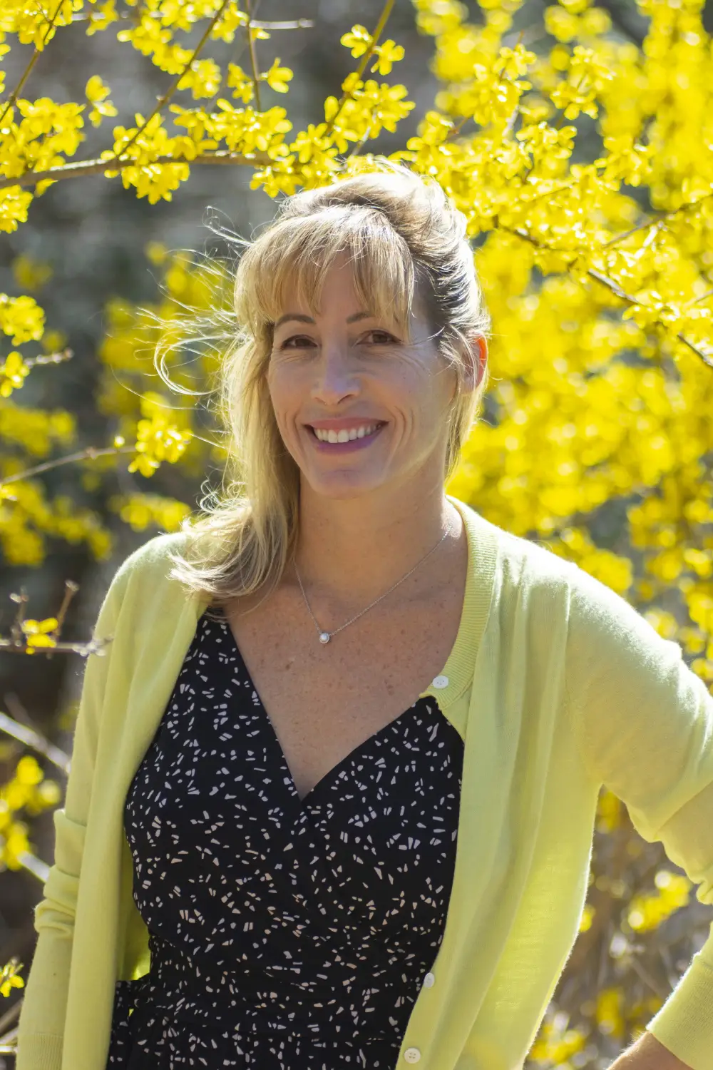 person in a black dress and yellow cardigan with a backdrop of yellow flowers